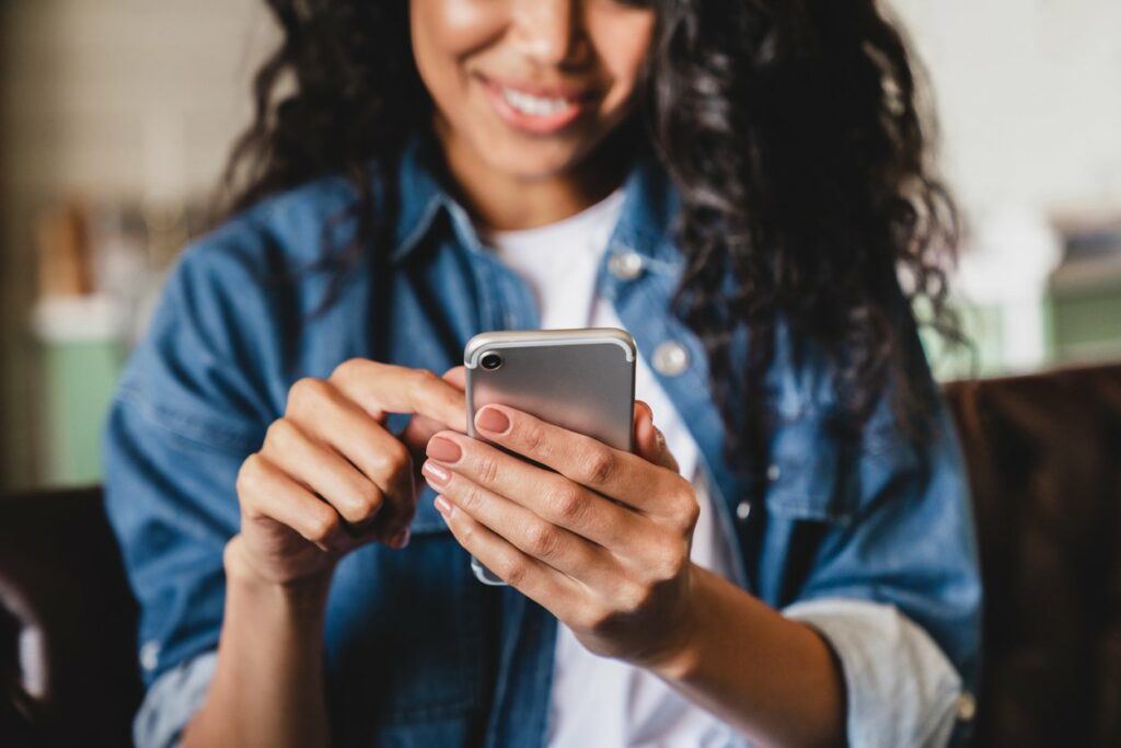 A woman holds a smartphone and scrolls while smiling at the screen