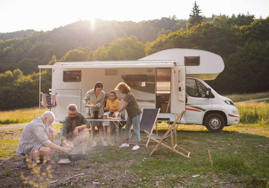 A family gathers outside of a camper at a folding table by a fire