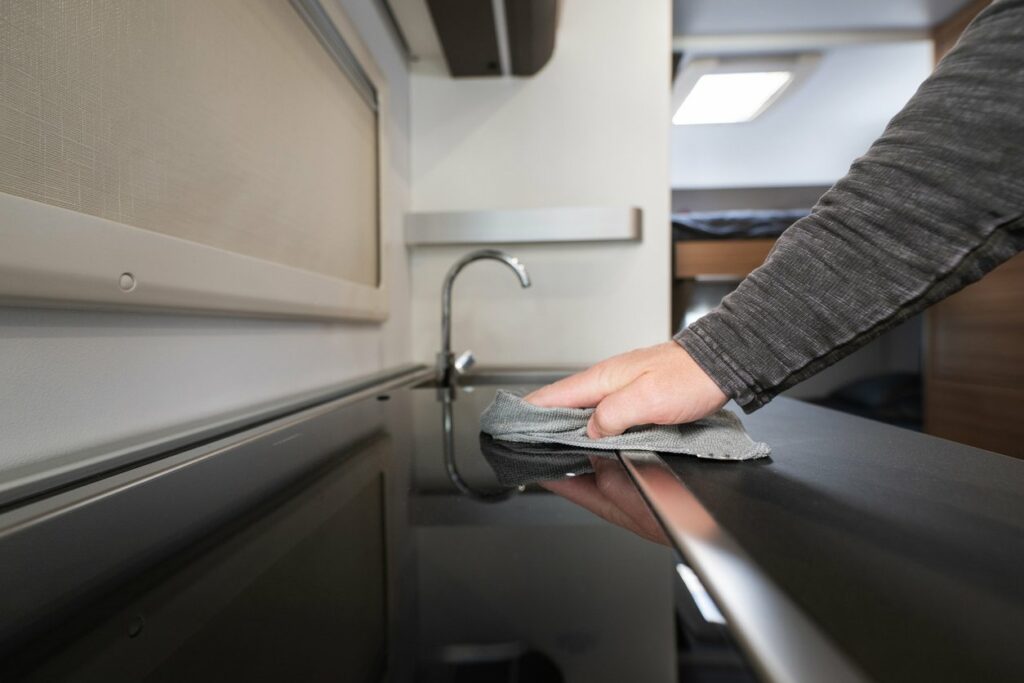 A man wipes down black countertops in a small kitchen space.