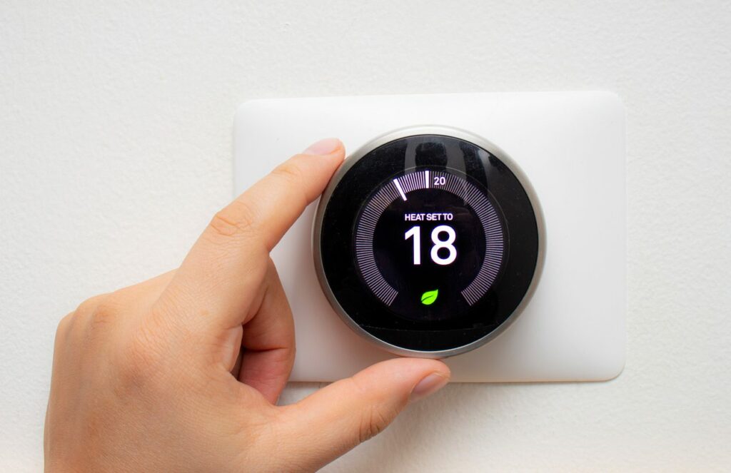 A person adjusts smart thermostat on wall.