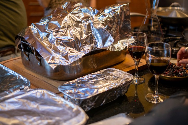 Several dishes on the table are wrapped or covered by aluminum foil to keep food warm