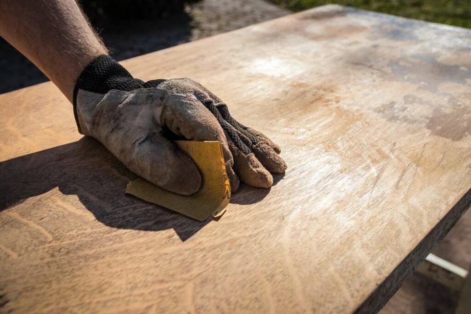 A man wearing a glove sands the top of a wooden desk