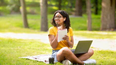 Woman sitting on green lawn with a laptop and notepad.