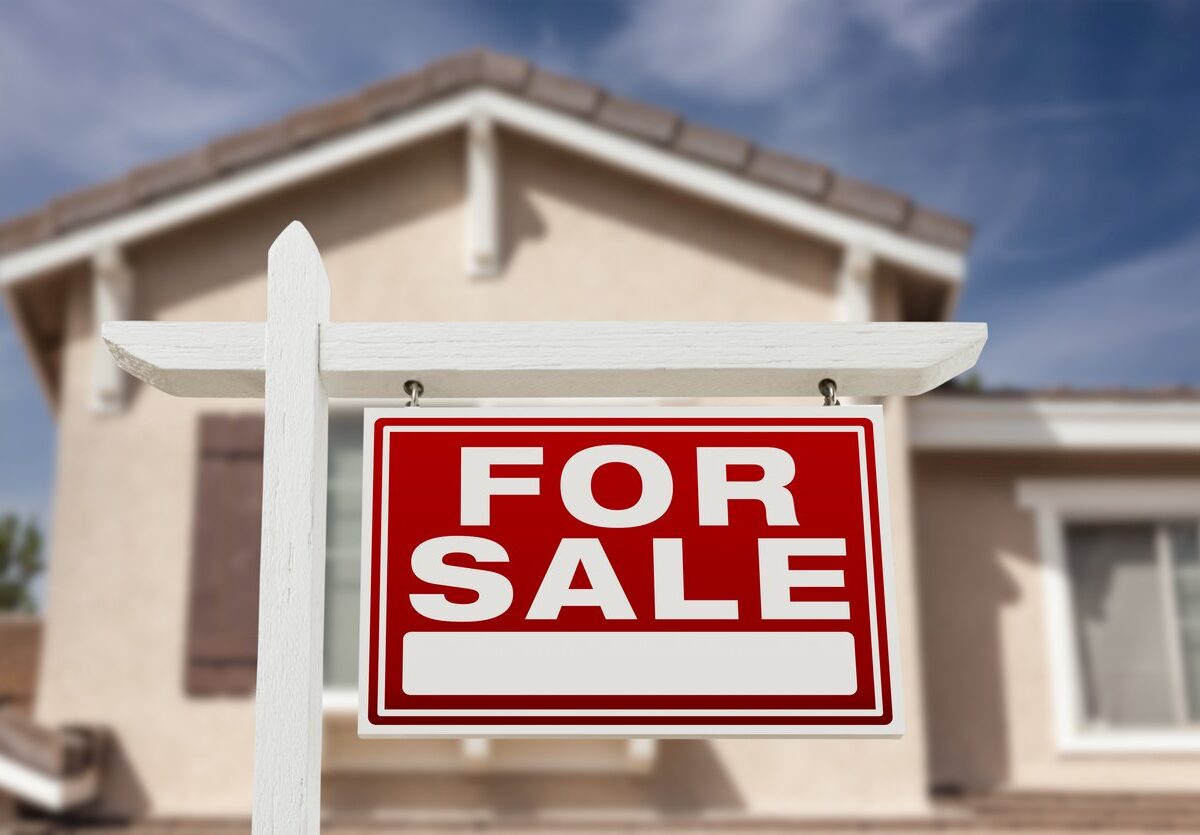 A red and white for sale sign in front of a house.
